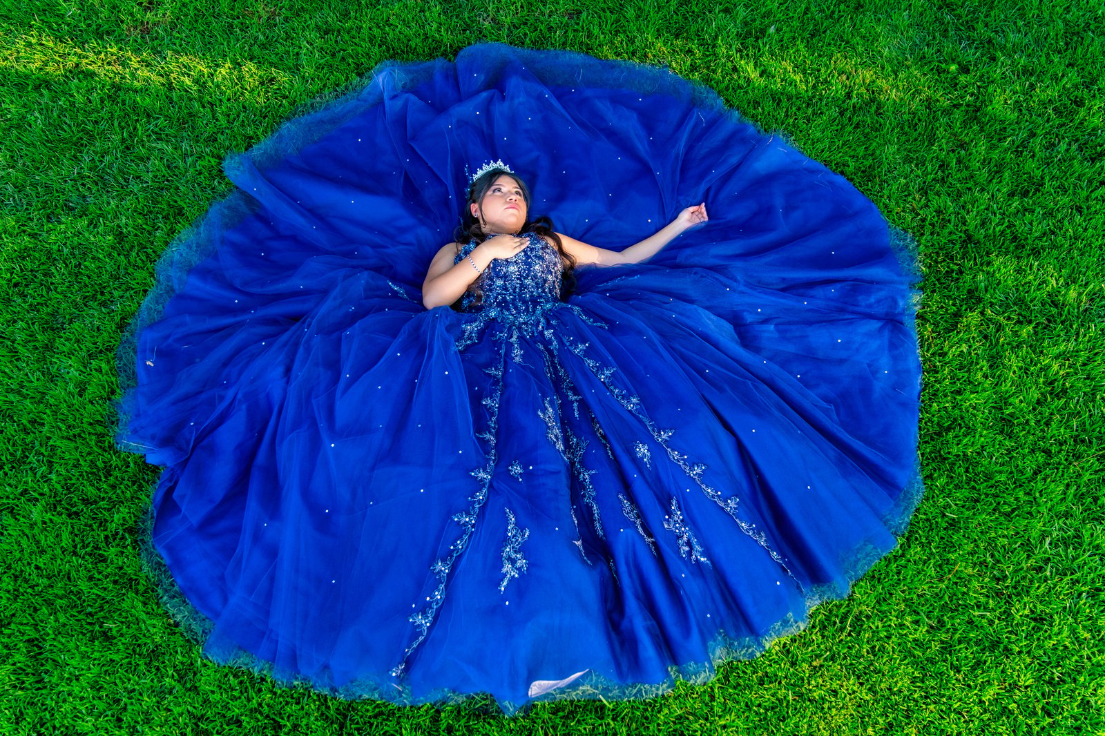 Blue quinceañera gown spread across the grass in an overhead portrait